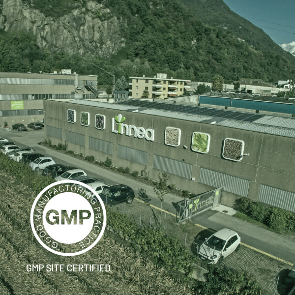 A picture of Linnea’s headquarters. Mountains can be seen. At the bottom right of the photo is a white circle. Following the shape around a solid circle the words read: Good Manufacturing Practice. Within the solid circle are the letters GMP. Beneath the circle the words read: GMP Site Certified.