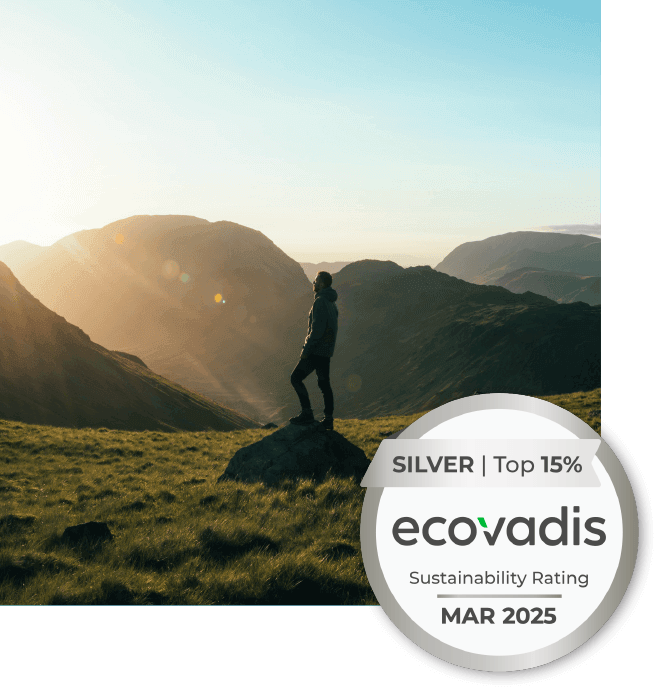 A person in the foreground that is standing on a rock in an open field with sun setting. There is a circular icon attached to the bottom right of the image that reads: SIlver 2022 Ecovadis Sustainability Rating.